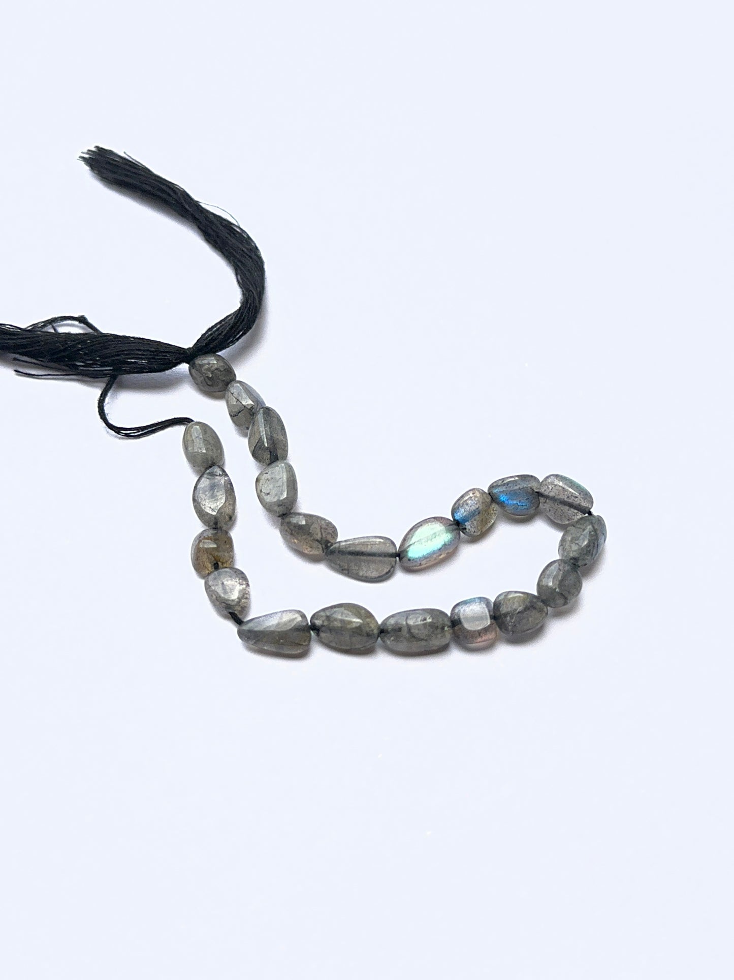 Labradorite smooth tumbled beads arranged on a strand, showing crisp organic and natural iridescence.