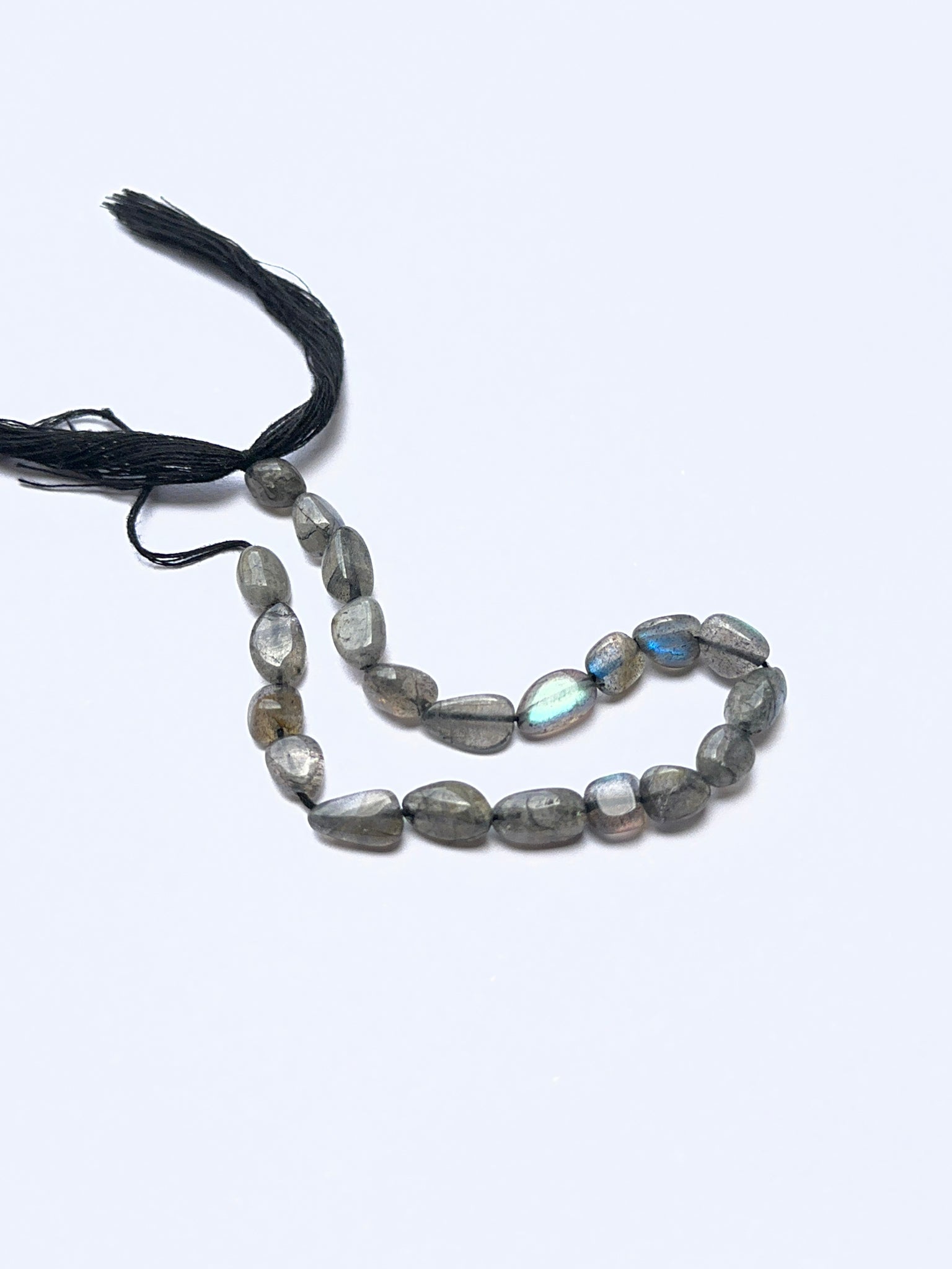 Labradorite smooth tumbled beads arranged on a strand, showing crisp organic and natural iridescence.