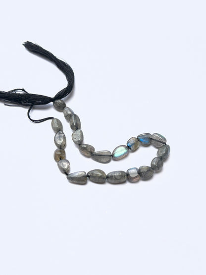 Labradorite smooth tumbled beads arranged on a strand, showing crisp organic and natural iridescence.
