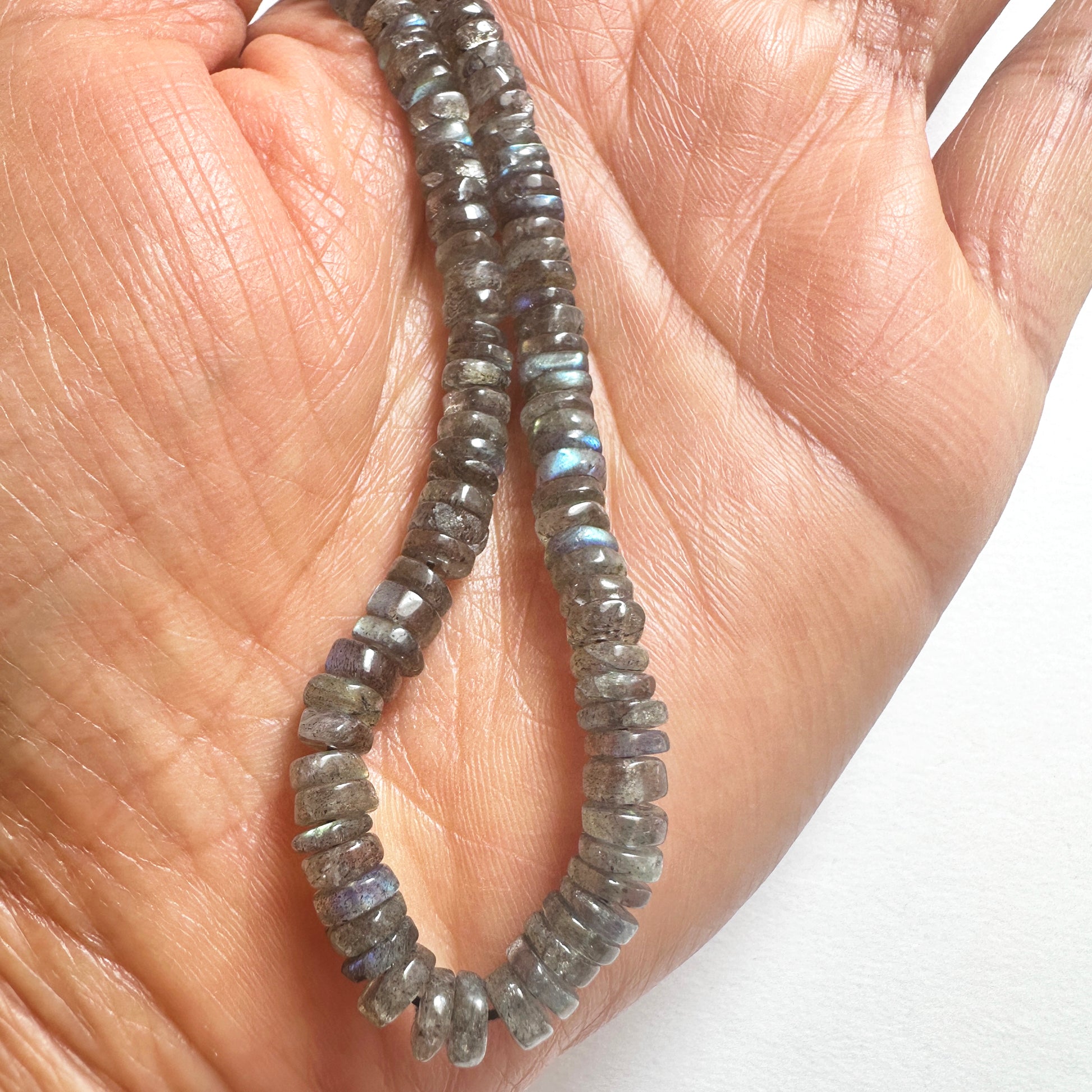 A person holds delicate strands of Labradorite beads, showcasing their smooth design.