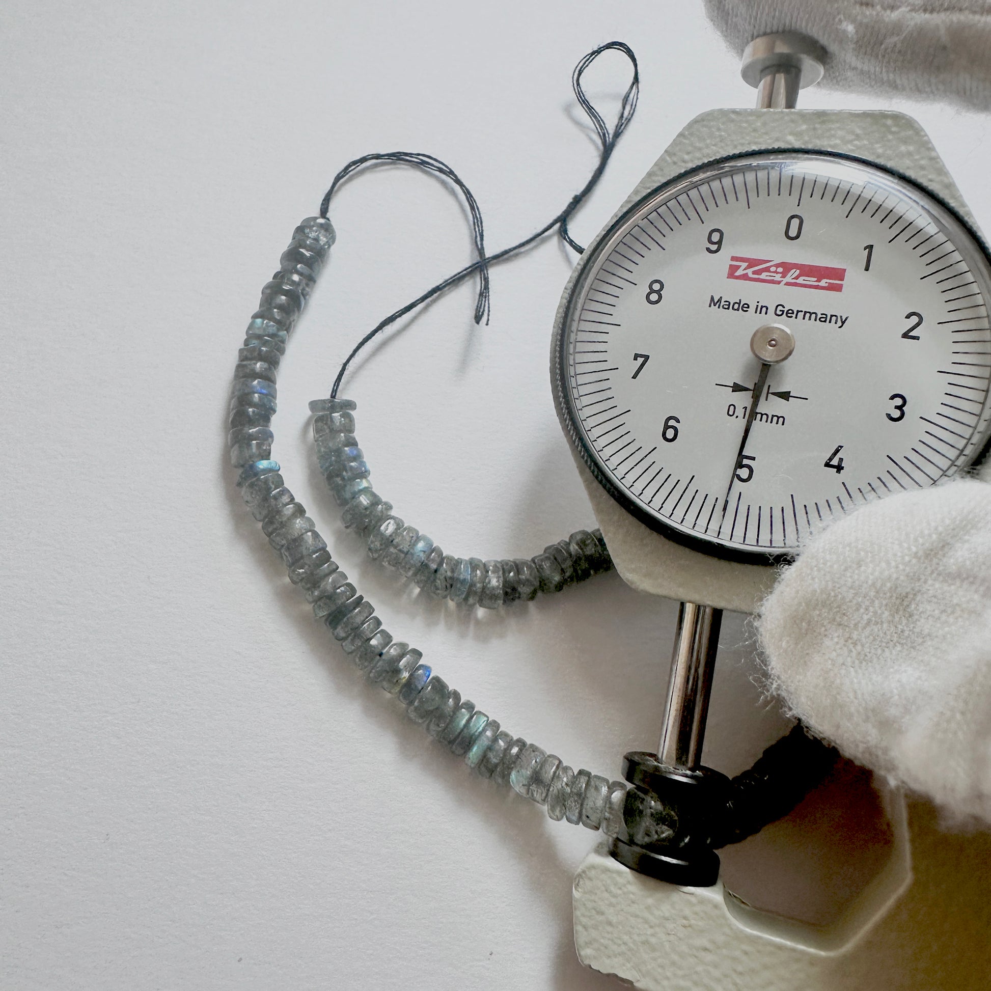 A dial gauge measures the Labradorite smooth wheel 5.1-5.4mm gemstone.