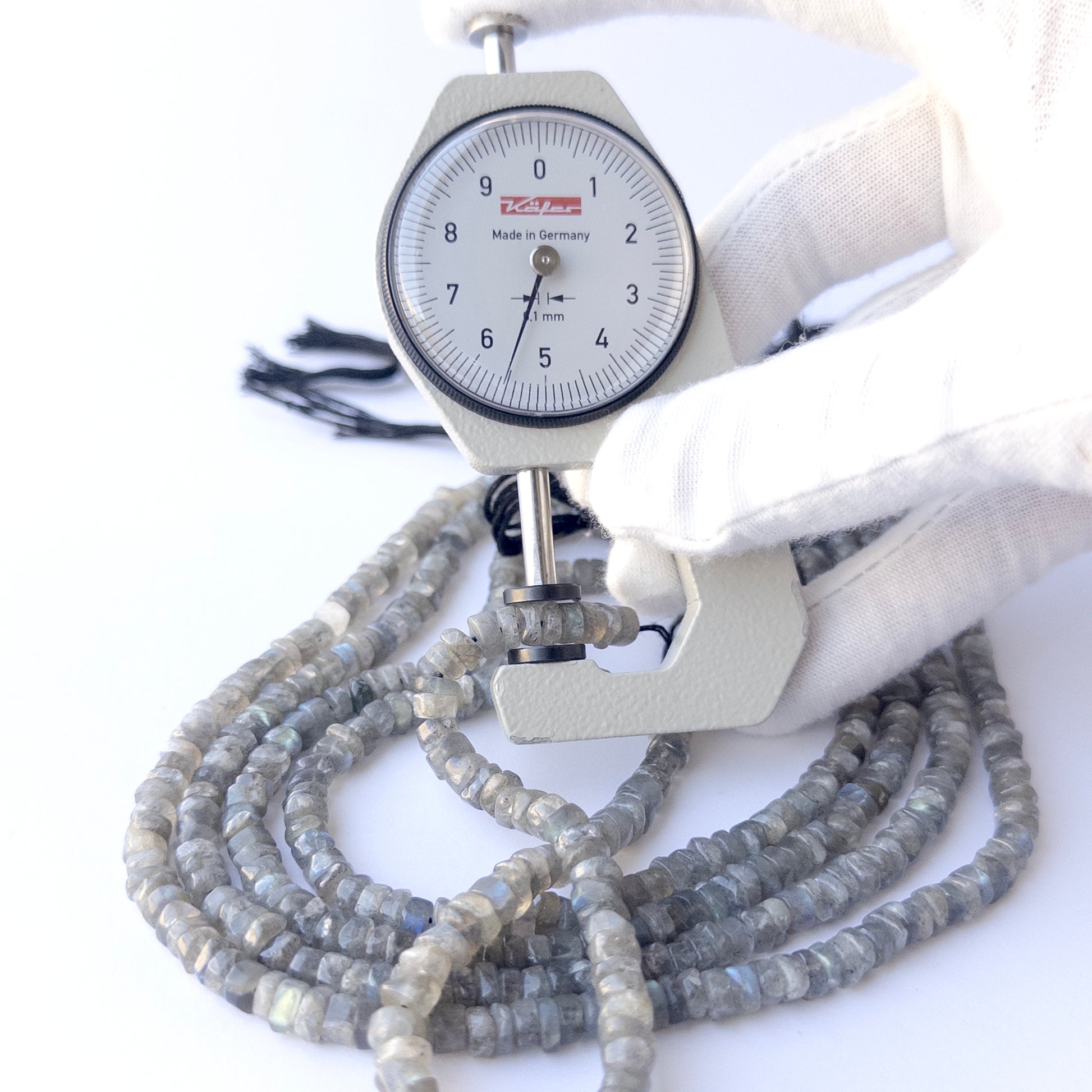 A dial gauge measures the Labradorite smooth wheel 5.3–5.6mm gemstone.
