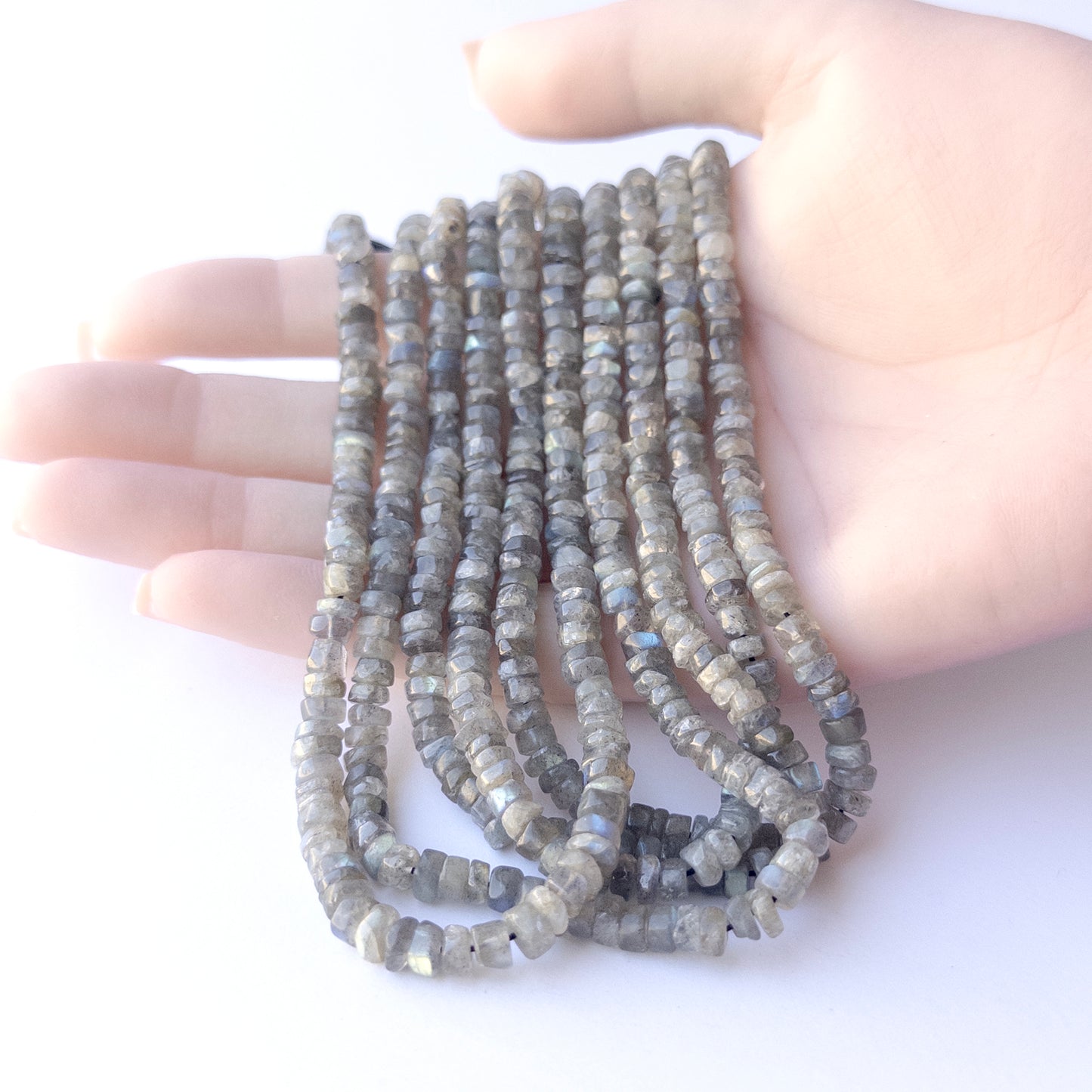 A person holds delicate strands of Labradorite beads, showcasing their smooth wheel design.