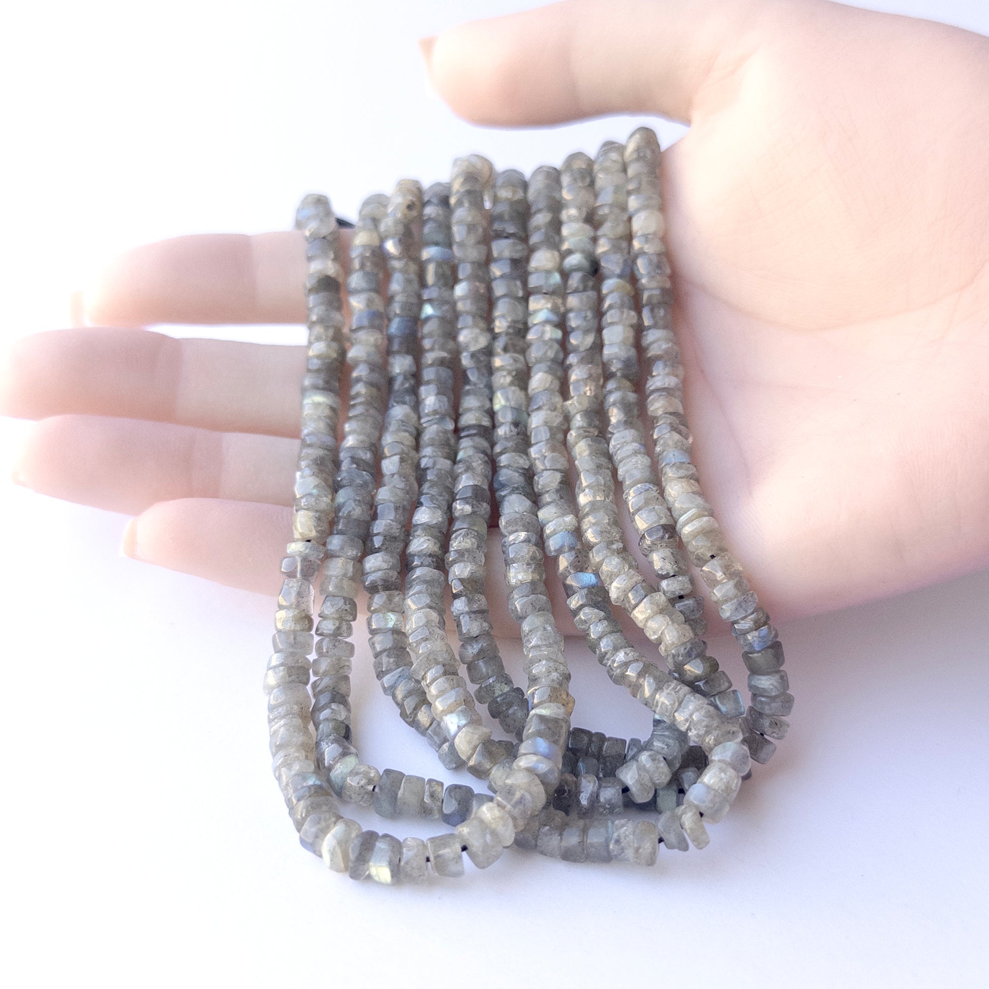 A person holds delicate strands of Labradorite beads, showcasing their smooth wheel design.