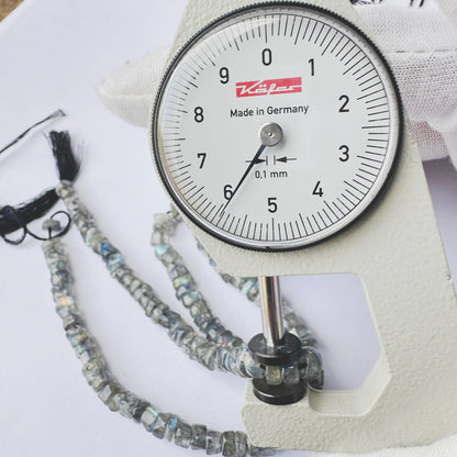 A dial gauge measures the Labradorite smooth wheel 5.5mm gemstone.