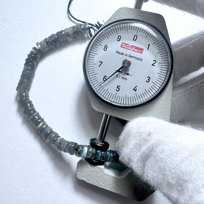 A dial gauge measures the Labradorite smooth wheel gemstone.