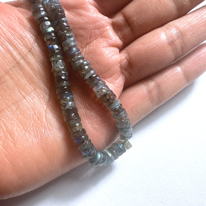 A person holds delicate strands of Labradorite beads, showcasing their design.