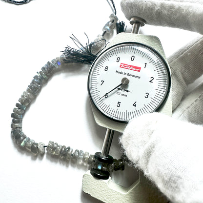 A dial gauge measures the Labradorite smooth wheel 6-6.2mm gemstone.