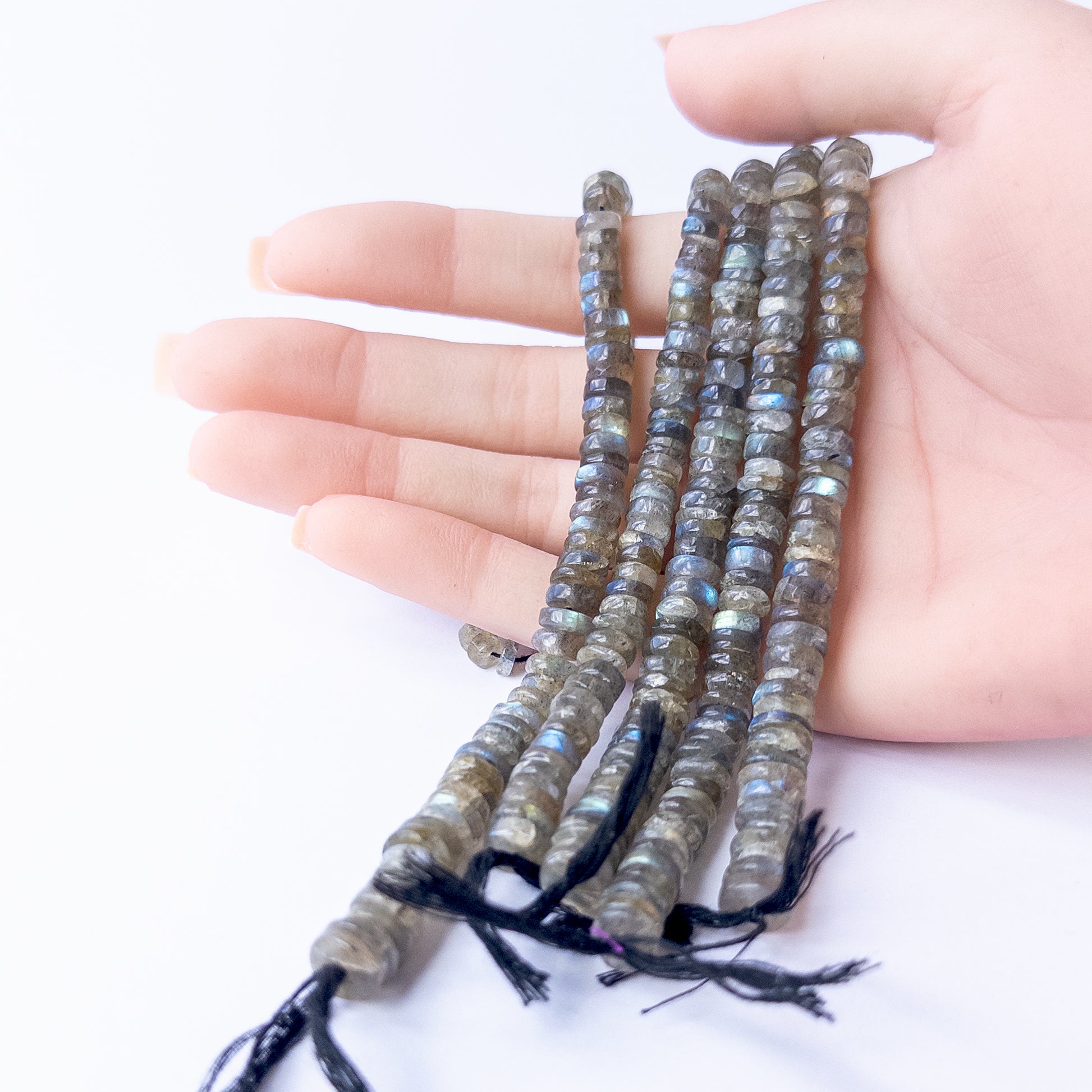 A person holds delicate strands of Labradorite smooth wheel beads, showcasing their polished design.