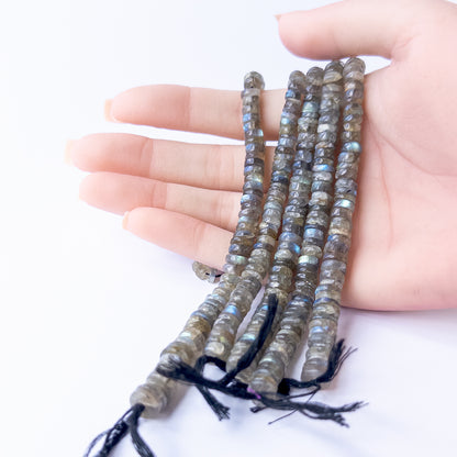 A person holds delicate strands of Labradorite smooth wheel beads, showcasing their polished design.