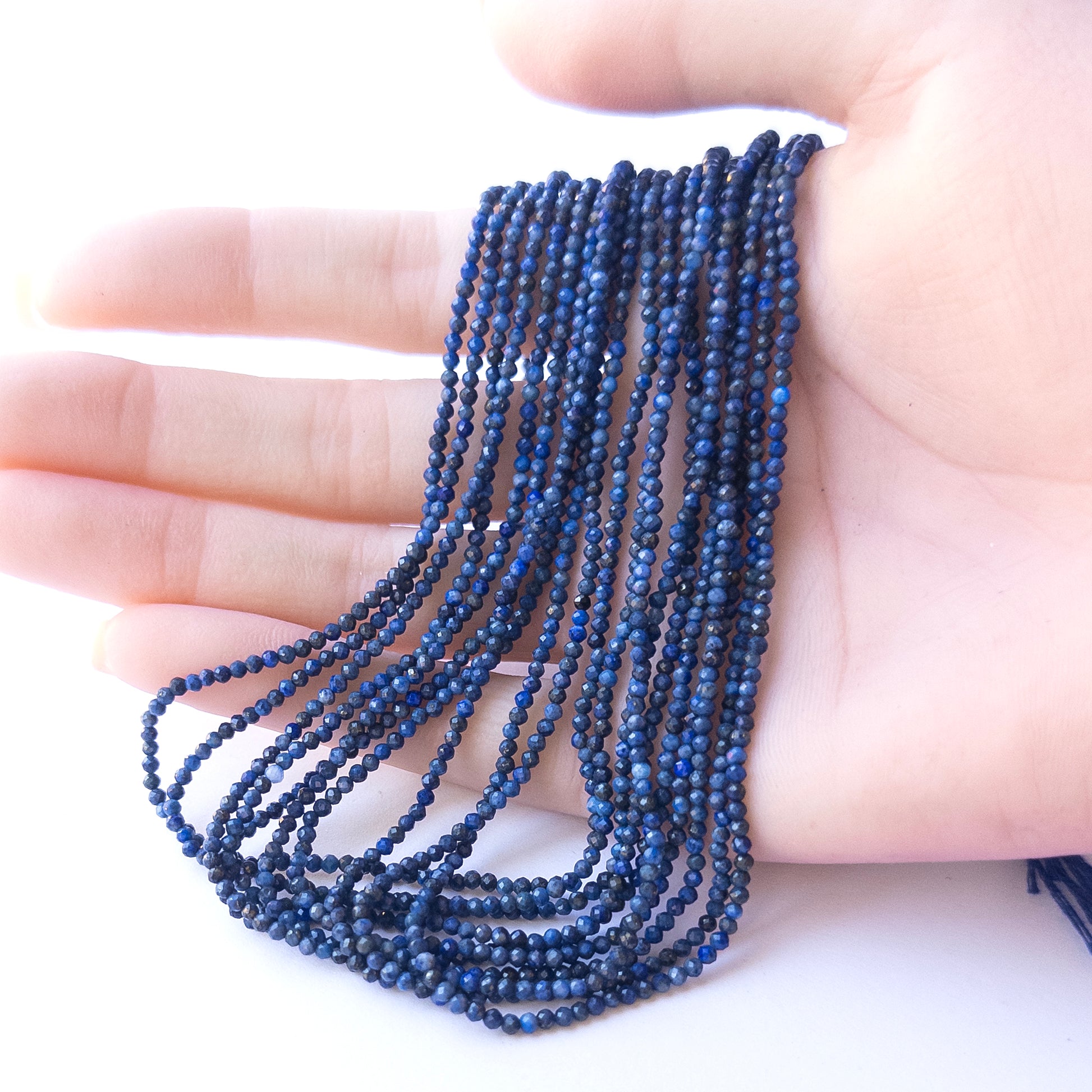 A person holds delicate strands of Lapis Lazuli beads, showcasing their Faceted Rondelle design.