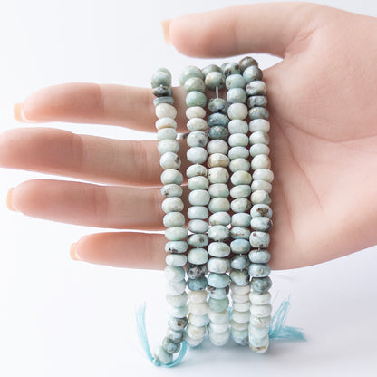 A person holds delicate strands of Larimar beads, showcasing their faceted rondelle design.