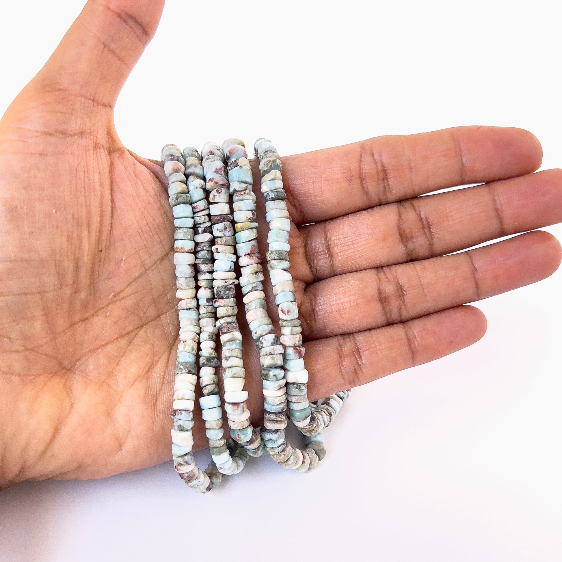 A person holds delicate strands of Larimar smooth wheel beads, showcasing their polished design.