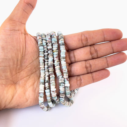 A person holds delicate strands of Larimar smooth wheel beads, showcasing their polished design.