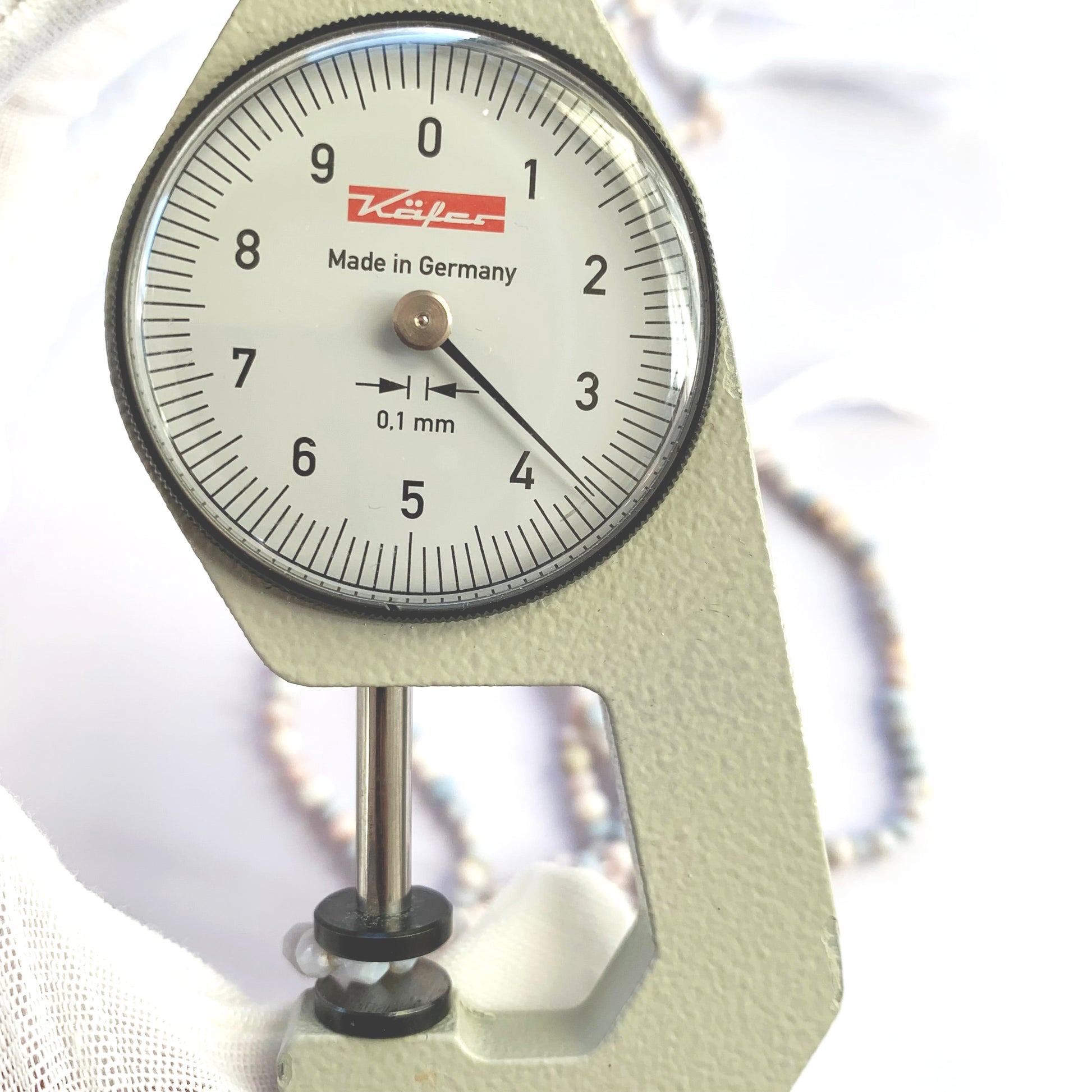 A dial gauge measures the Lavender Opal faceted rondelle 3.5-4mm gemstone.