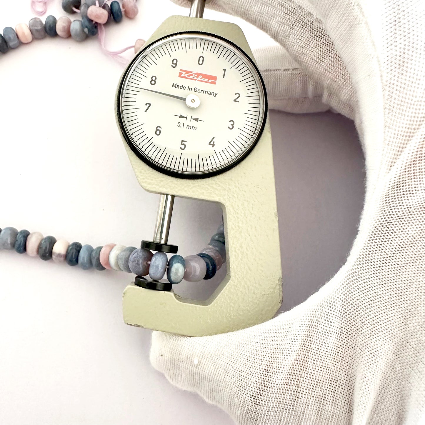 A person holds delicate strands of Lavender Opal beads, showcasing their smooth design.
