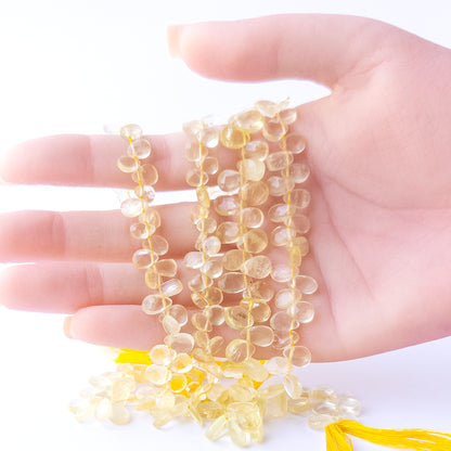 A person holds delicate strands of Lemon Quartz beads, showcasing their faceted briolette design.