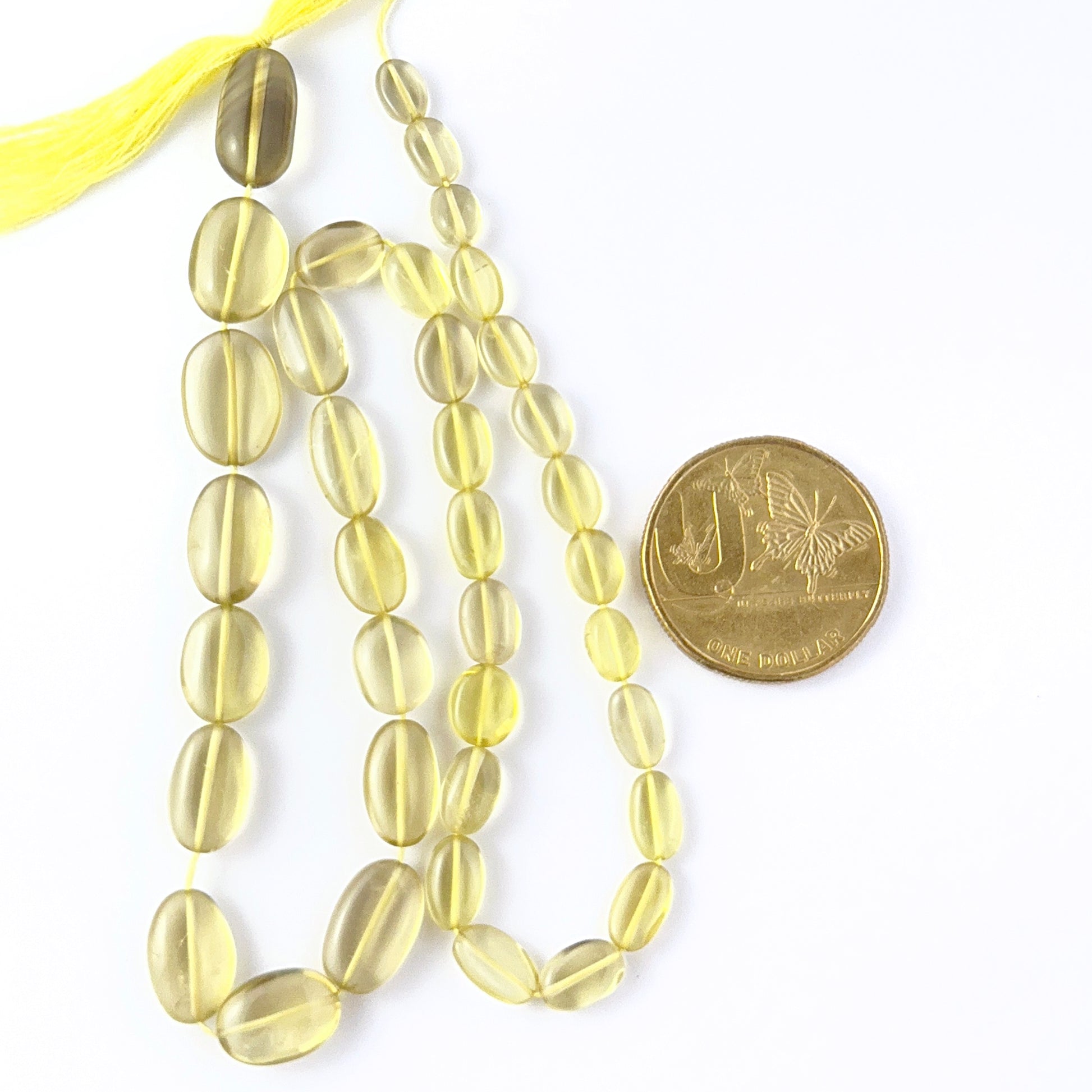 A coin is placed near delicate strands of Lemon Quartz beads for scale