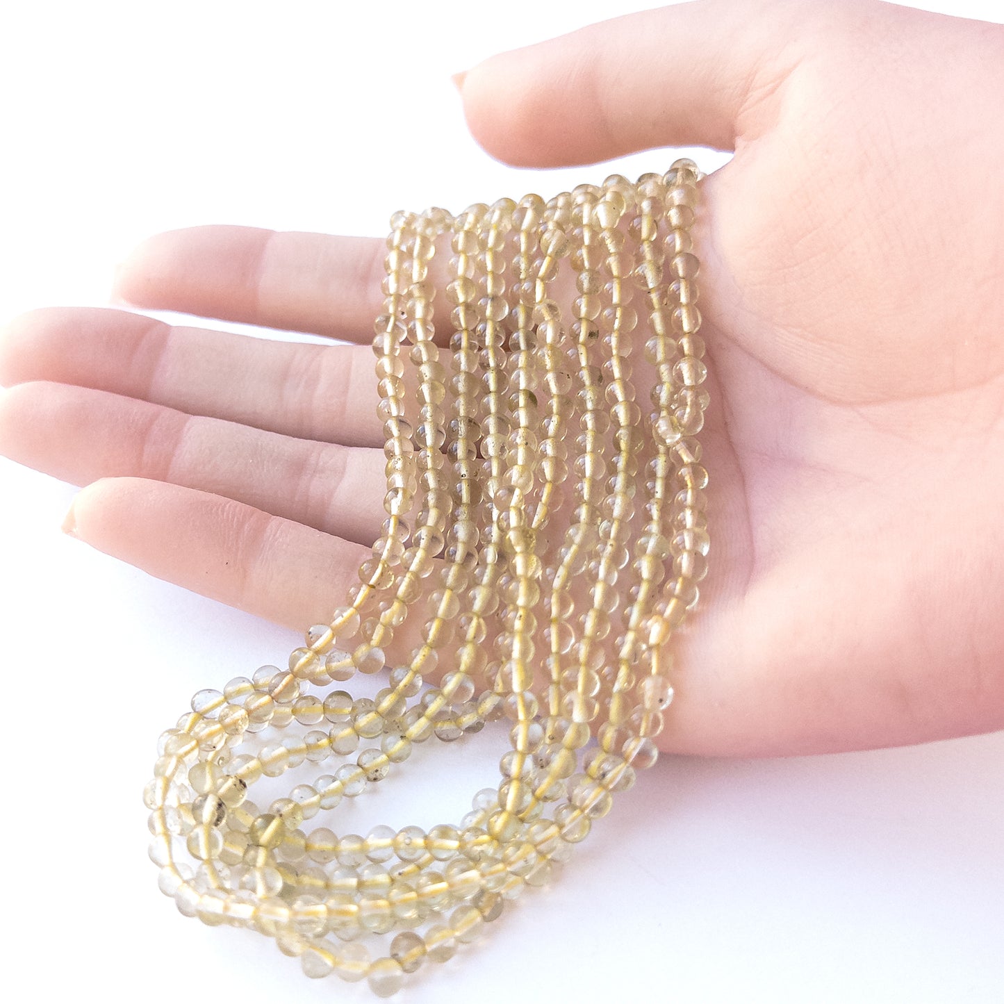 A person holds delicate strands of Lemon Quartz beads, showcasing their smooth round design.