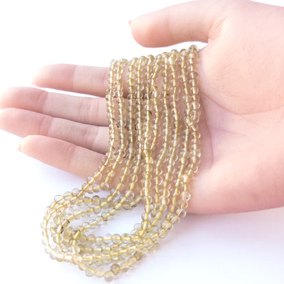 A person holds delicate strands of Lemon Quartz beads, showcasing their smooth round design.