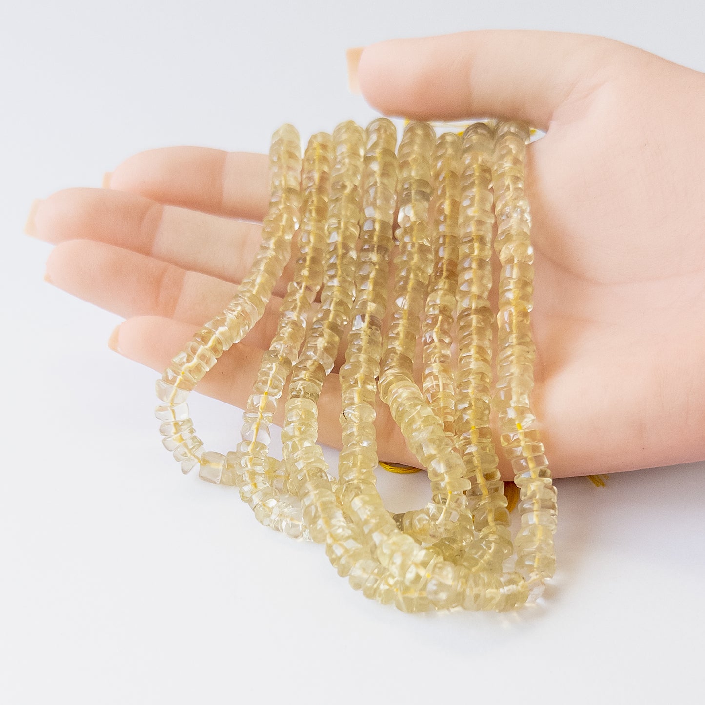 A person holds delicate strands of Lemon Quartz beads, showcasing their smooth wheel design.