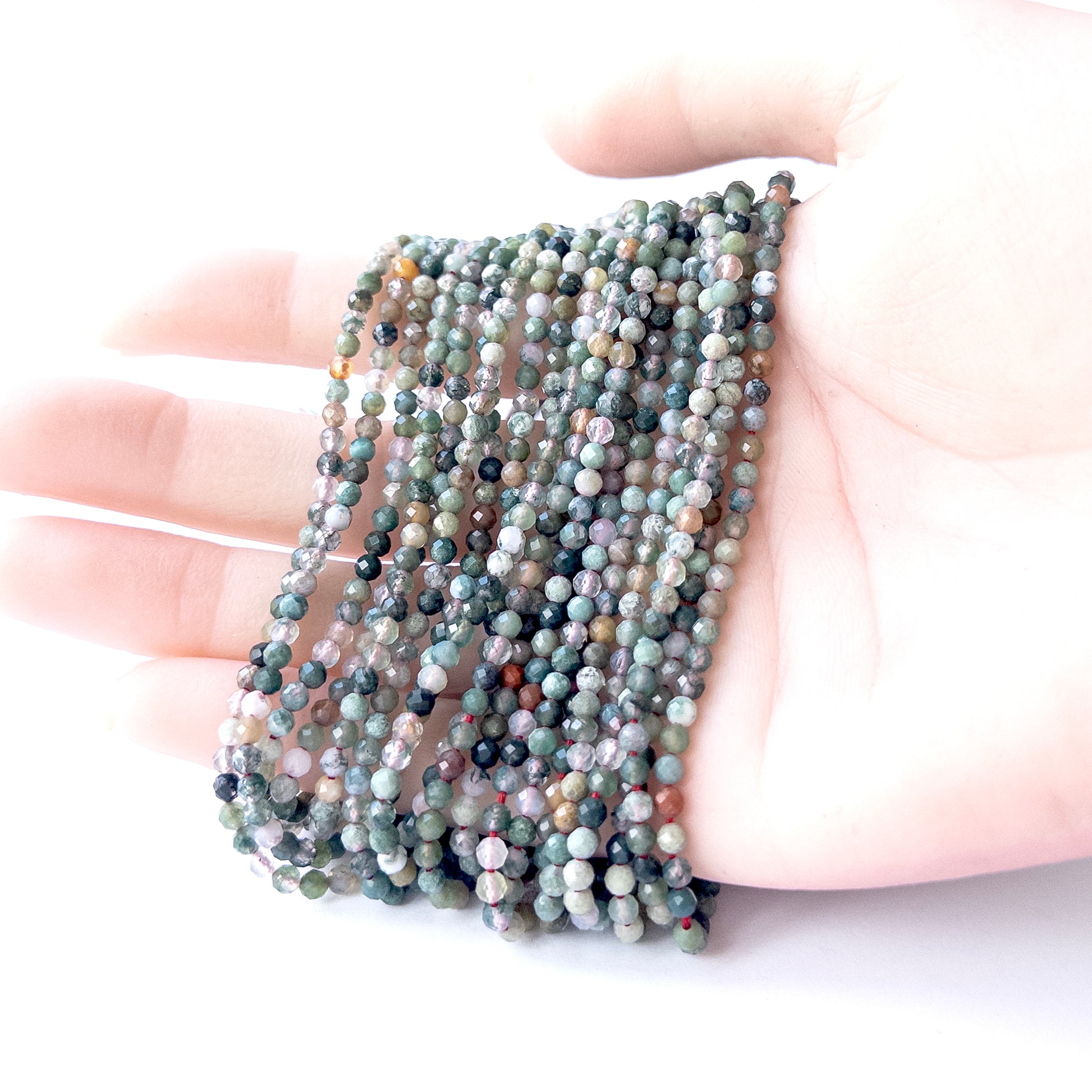 A person holds delicate strands of Mixed Agate beads, showcasing their faceted rondelle design.