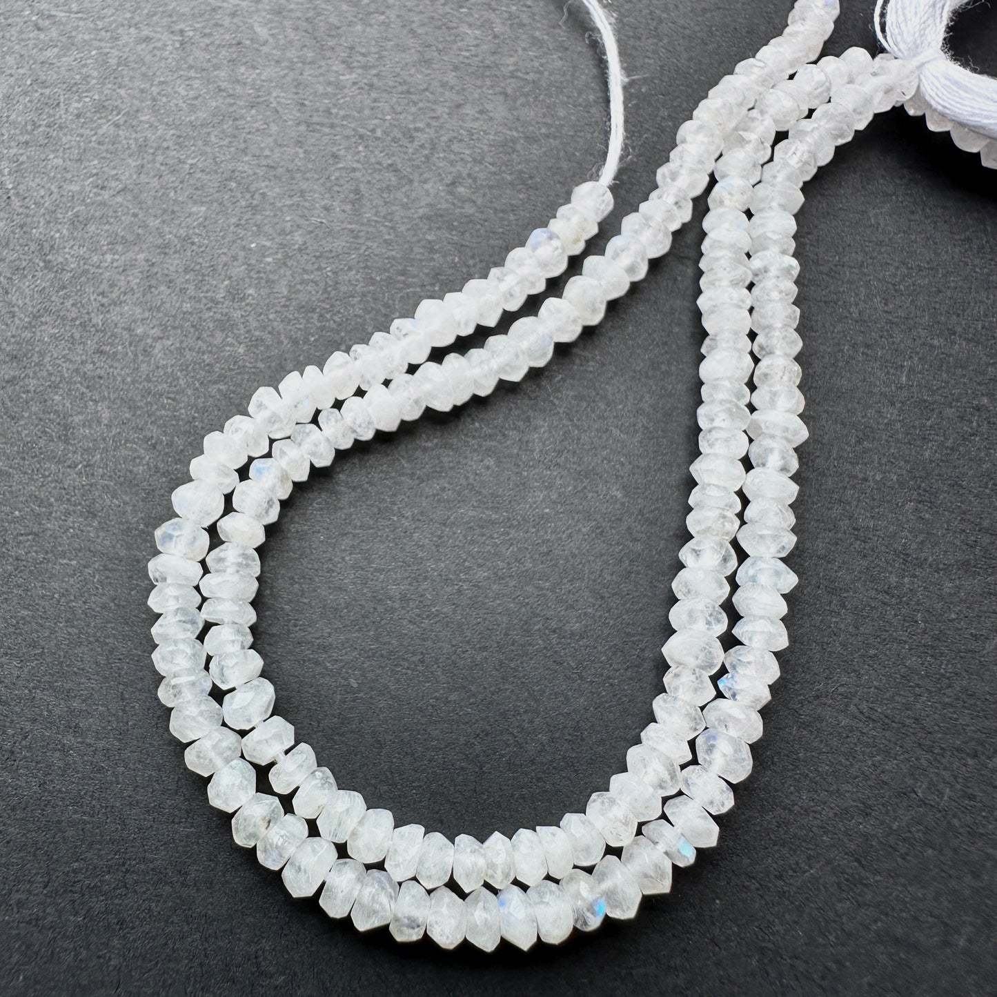 Moonstone faceted rondelle beads with pearly white tones and blue flashes arranged on a 13cm strand for jewellery making.
