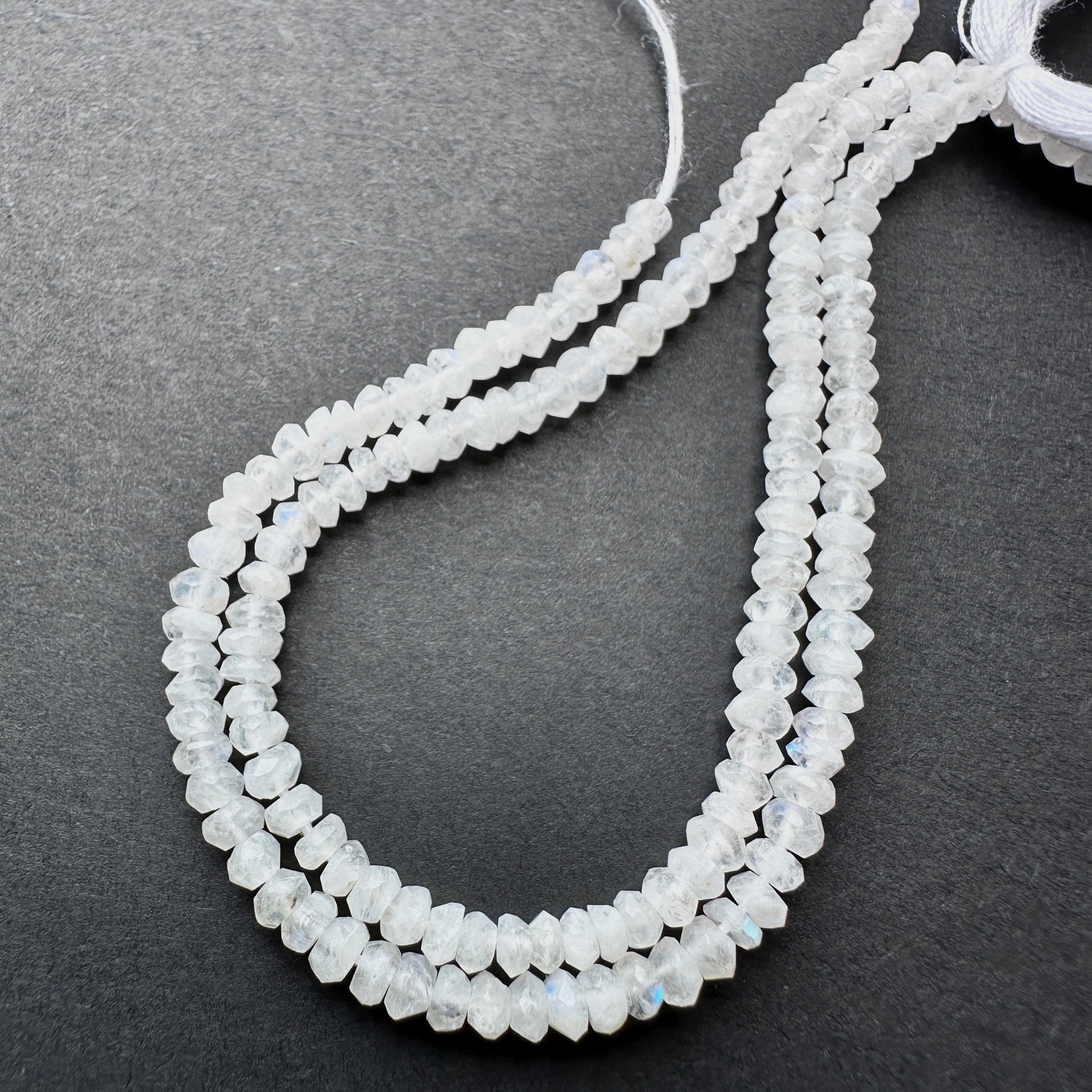 Moonstone faceted rondelle beads with pearly white tones and blue flashes arranged on a 13cm strand for jewellery making.