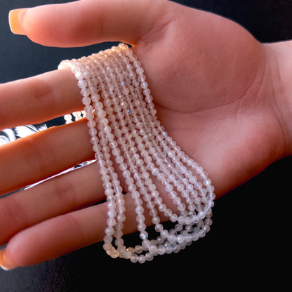 A person holds delicate strands of Moonstone beads, showcasing their faceted rondelle design.