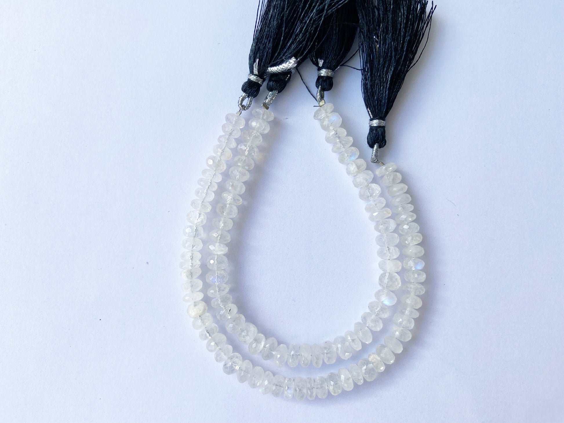 Glistening Moonstone beads with faceted surface aligned in uniform rows for jewellery crafting.