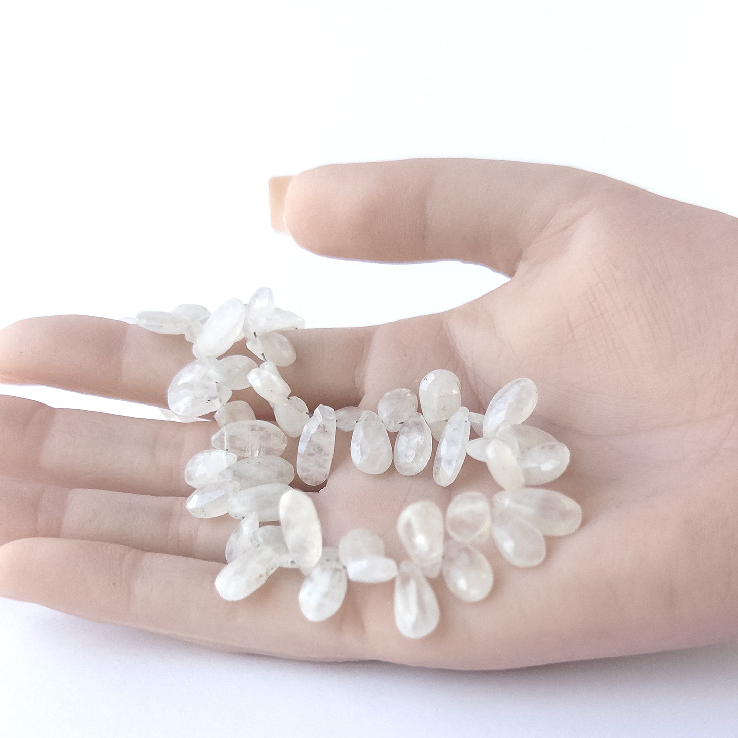A person holds delicate strands of Rainbow Moonstone beads, showcasing their faceted briolette design.