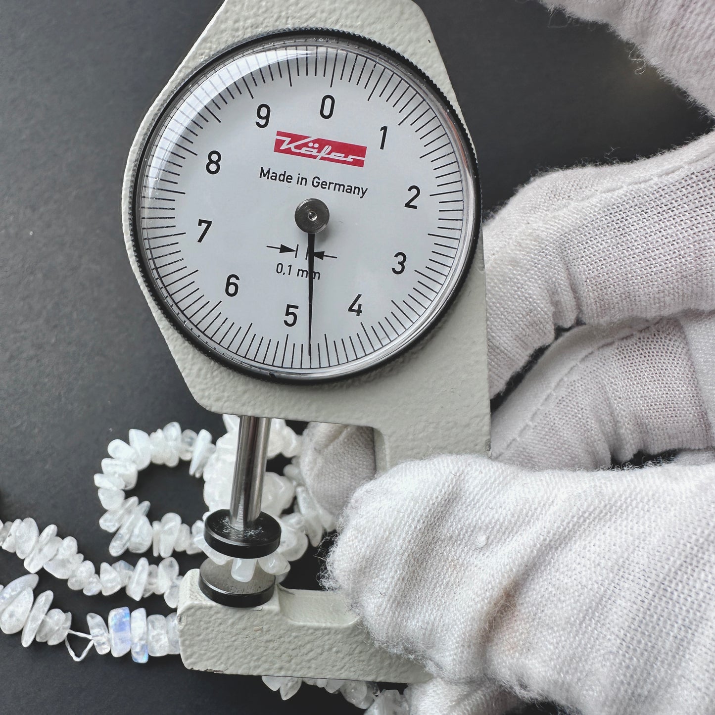 A dial gauge measures the Moonstone smooth chip 4-6mm gemstone.