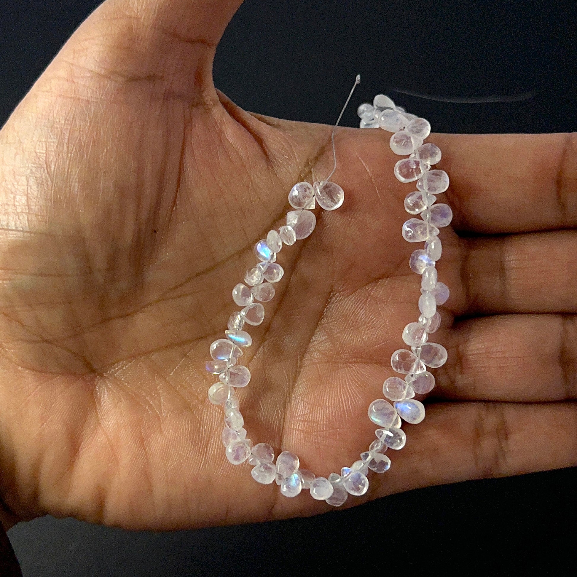 A person holds delicate strands of Moonstone beads, showcasing their smooth teardrop design.
