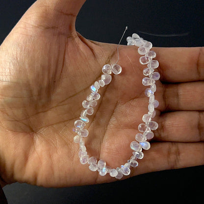 A person holds delicate strands of Moonstone beads, showcasing their smooth teardrop design.