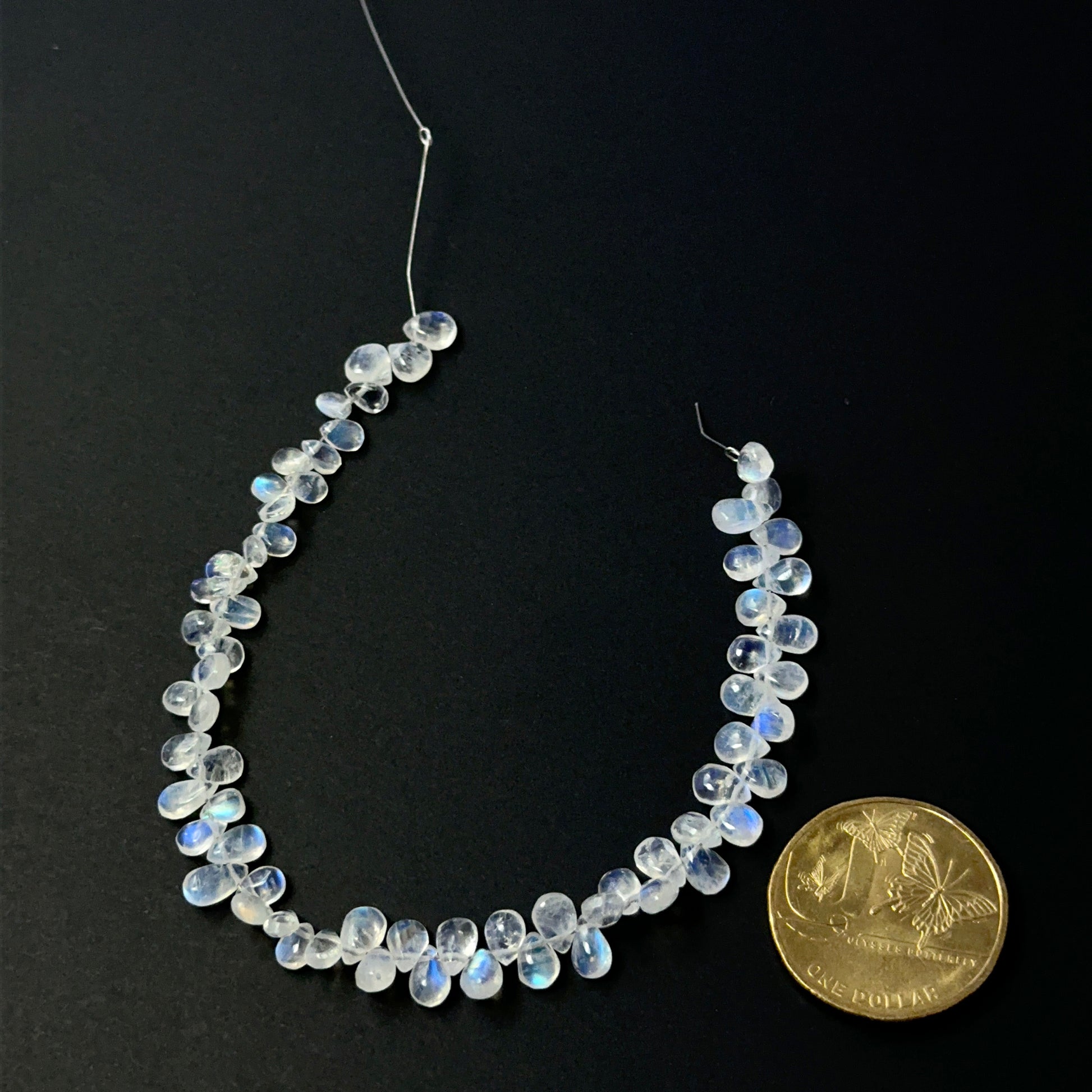 A coin is place near delicate strands of Moonstone beads for scale.