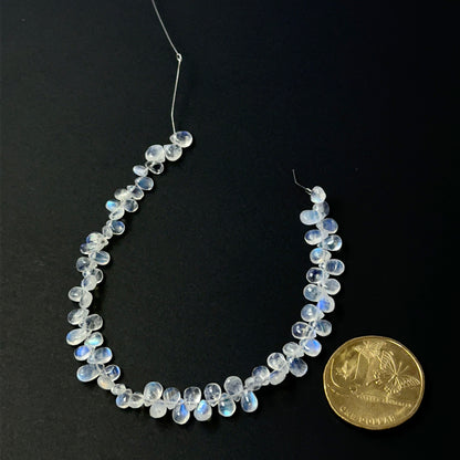 A coin is place near delicate strands of Moonstone beads for scale.