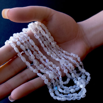 A person holds delicate strands of Moonstone beads, showcasing their smooth tumble design.