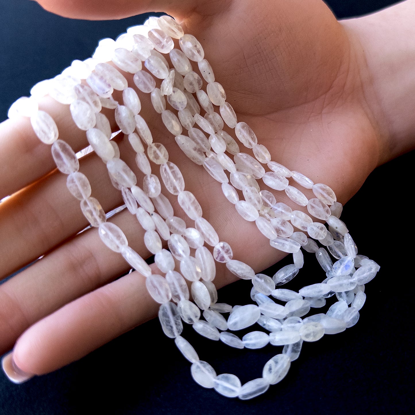 A person holds delicate strands of Moonstone beads, showcasing their smooth tumble design.