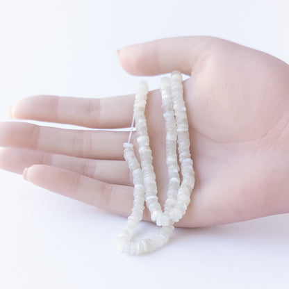 A person holds delicate strands of Moonstone beads, showcasing their smooth wheels design.