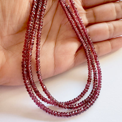 A person holds delicate strands of Mozambique Garnet beads, showcasing their faceted design.