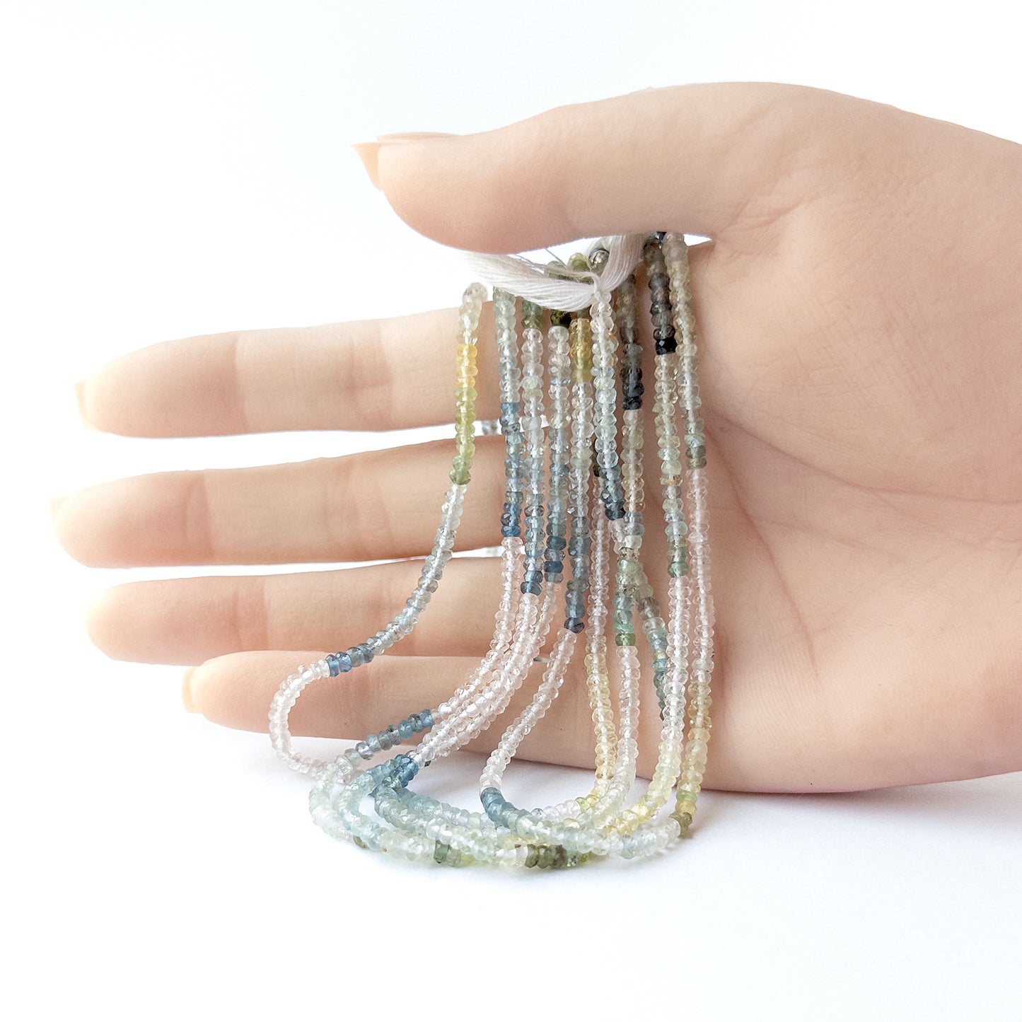 A person holds delicate strands of Multi Aquamarine beads, showcasing their faceted rondelle design.
