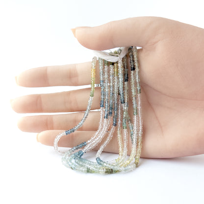 A person holds delicate strands of Multi Aquamarine beads, showcasing their faceted rondelle design.