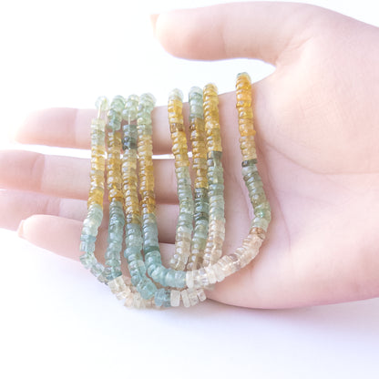 A person holds delicate strands of Multi Aquamarine beads, showcasing their smooth wheels heishi design.  