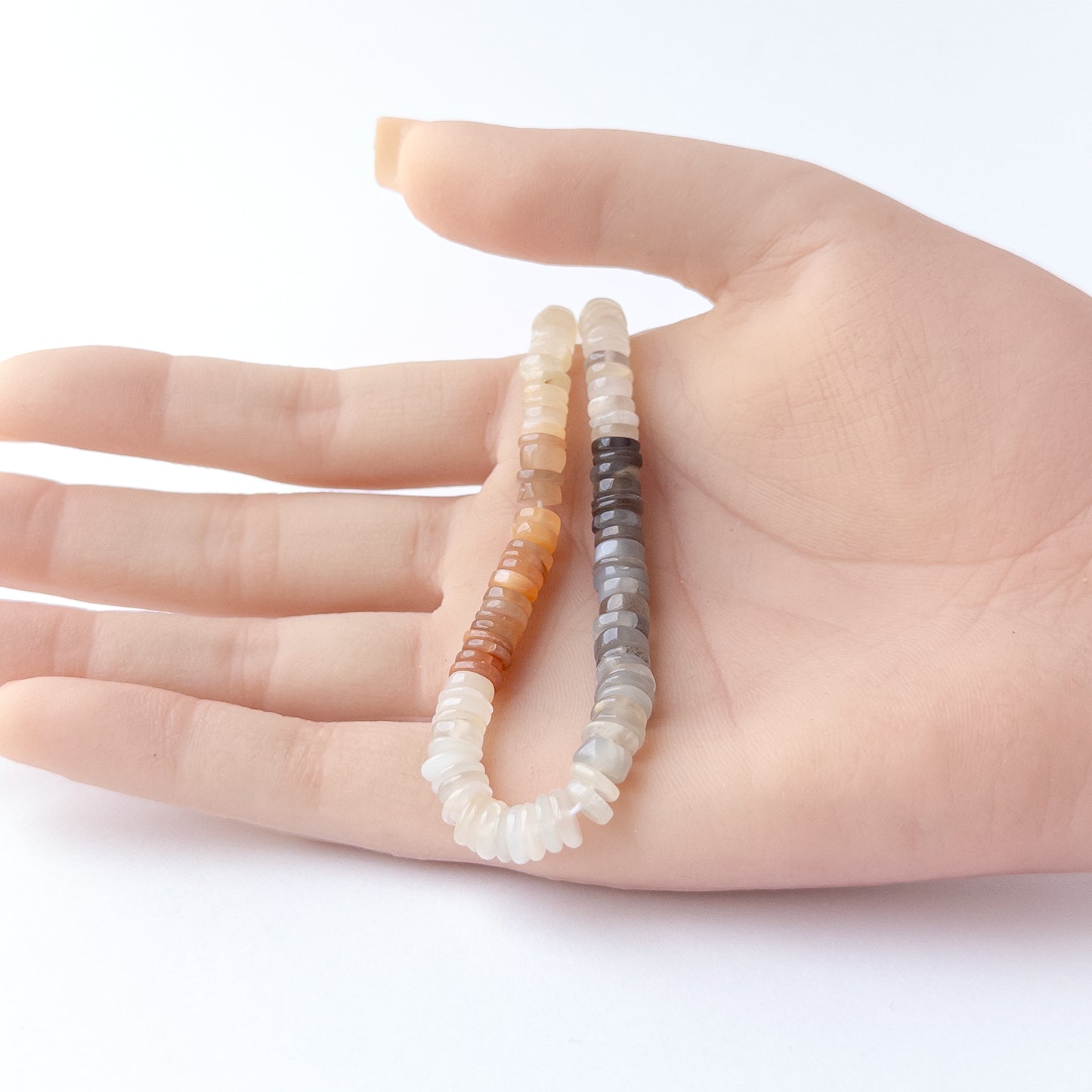 A person holds delicate strands of Multi Moonstone beads, showcasing their smooth wheel design.