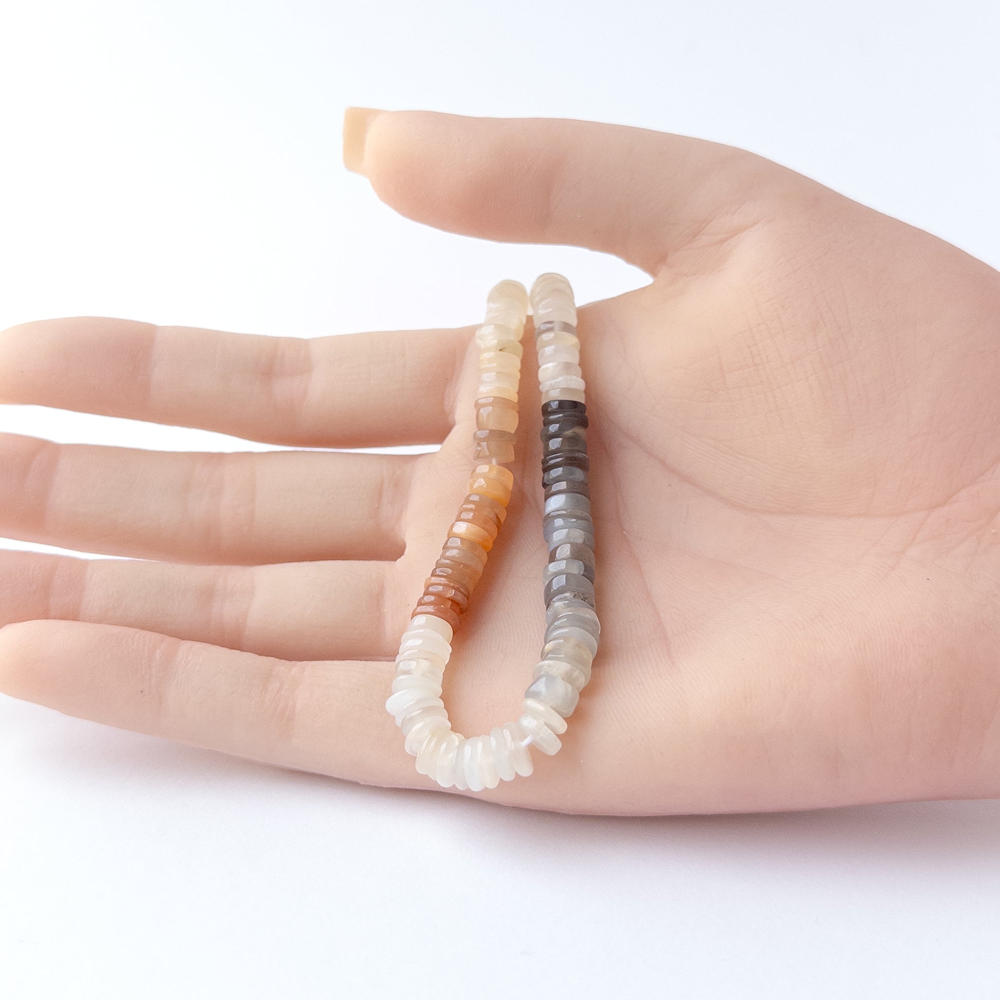 A person holds delicate strands of Multi Moonstone beads, showcasing their smooth wheel design.