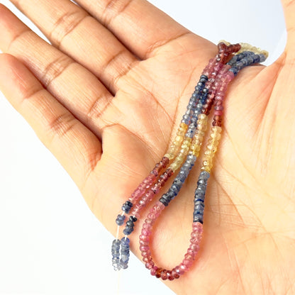 A person holds delicate strands of Multi Precious beads, showcasing their faceted rondelle design.