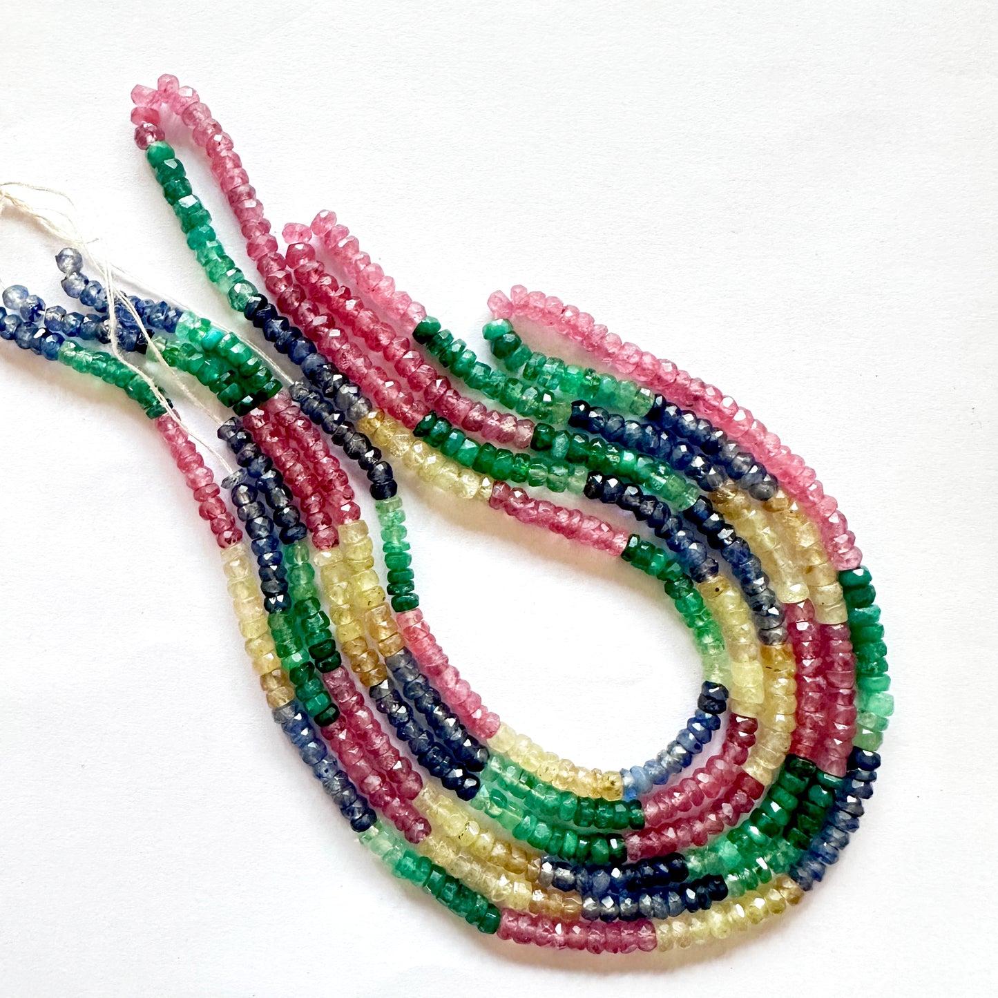 Sparkling rubies, emeralds yellow & blue sapphire faceted beads displayed in a polished gemstone layout.