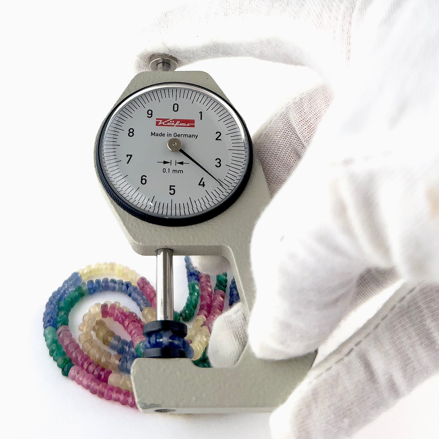A dial gauge measures the multi precious faceted rondelle 3.5–4mm gemstone.