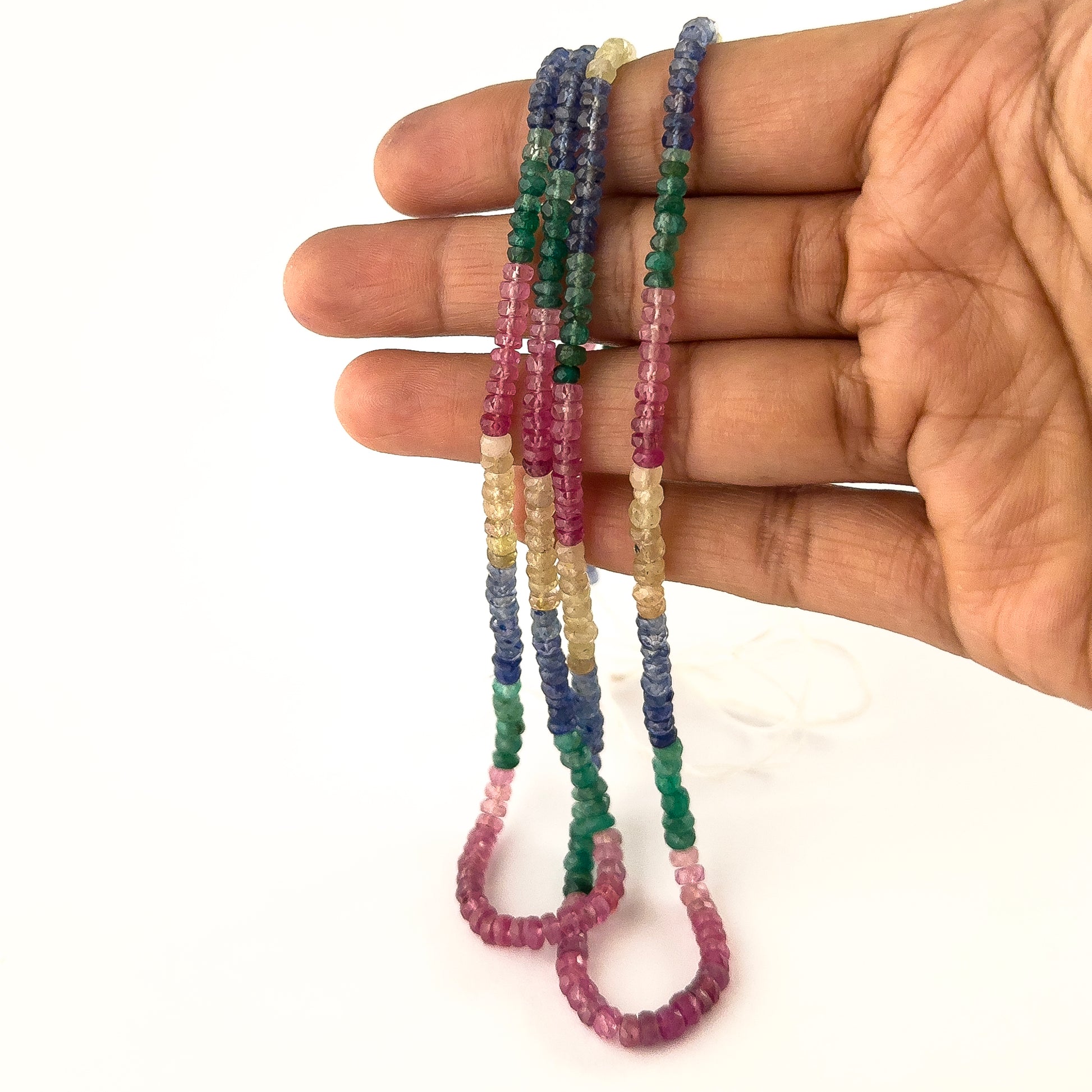 A person holds multi precious gemstone rondelle beads, showing their faceted design and colour variation.