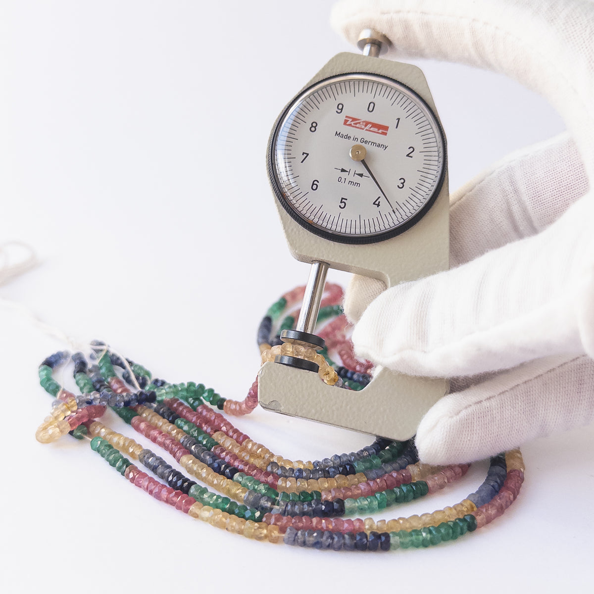 A person holds delicate strands of Multi Precious beads, showcasing their faceted rondelle design.